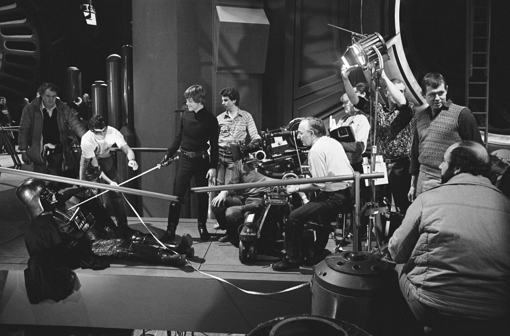 Mark Hamill is filmed during Luke’s moment of choice: Will he commit patricide or become a true Jedi and show compassion for his father (Simon Hume stands beside Hamill; assistant camera loader Tony Jackson, in white T-shirt, uses his tape measure; director Richard Marquand is on far right of image; Alec Mills operates the camera; holding the script pages is script supervisor Pamela Mann-Francis; in the foreground is Frank Elliott, bearded; Alan Hume adjusts the light). 